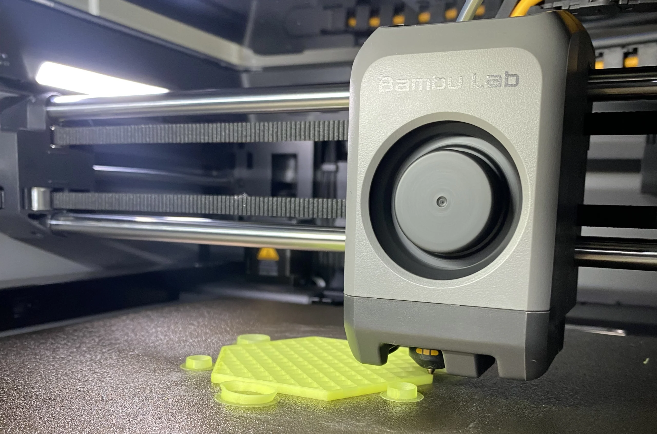 A 3D printer from Bambu Lab in action, printing a bright yellow hexagonal object. The scene is well-lit, highlighting precision and innovation.